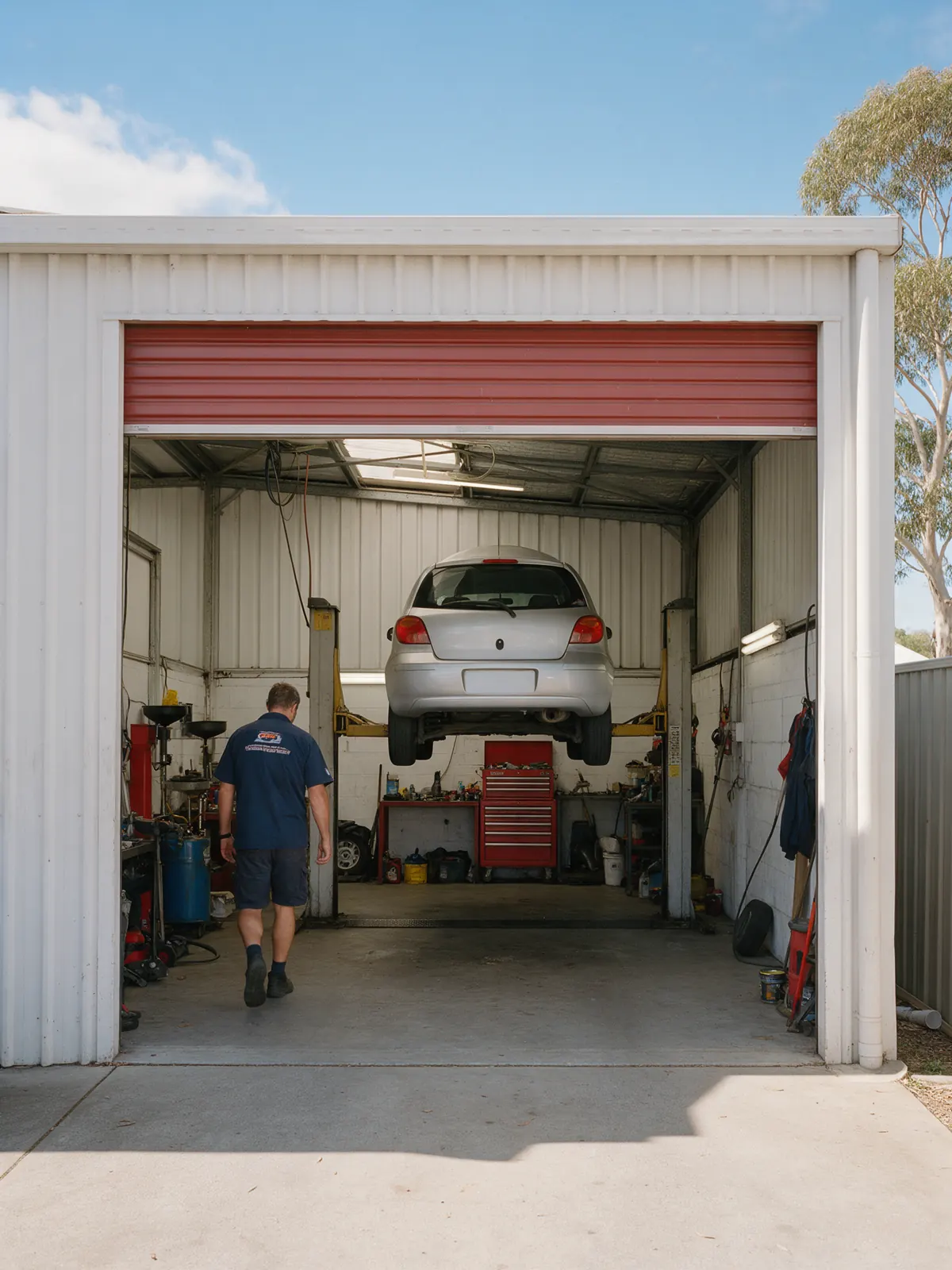 The workshop from the driveway, roller door up and a car on the hoist